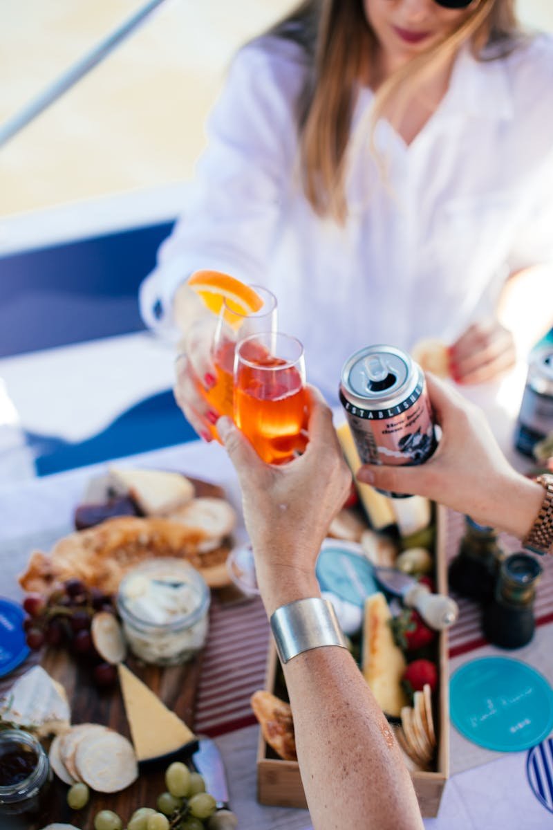 From above of crop anonymous friends in summer wear clinking glasses of alcoholic drinks while having party on boat